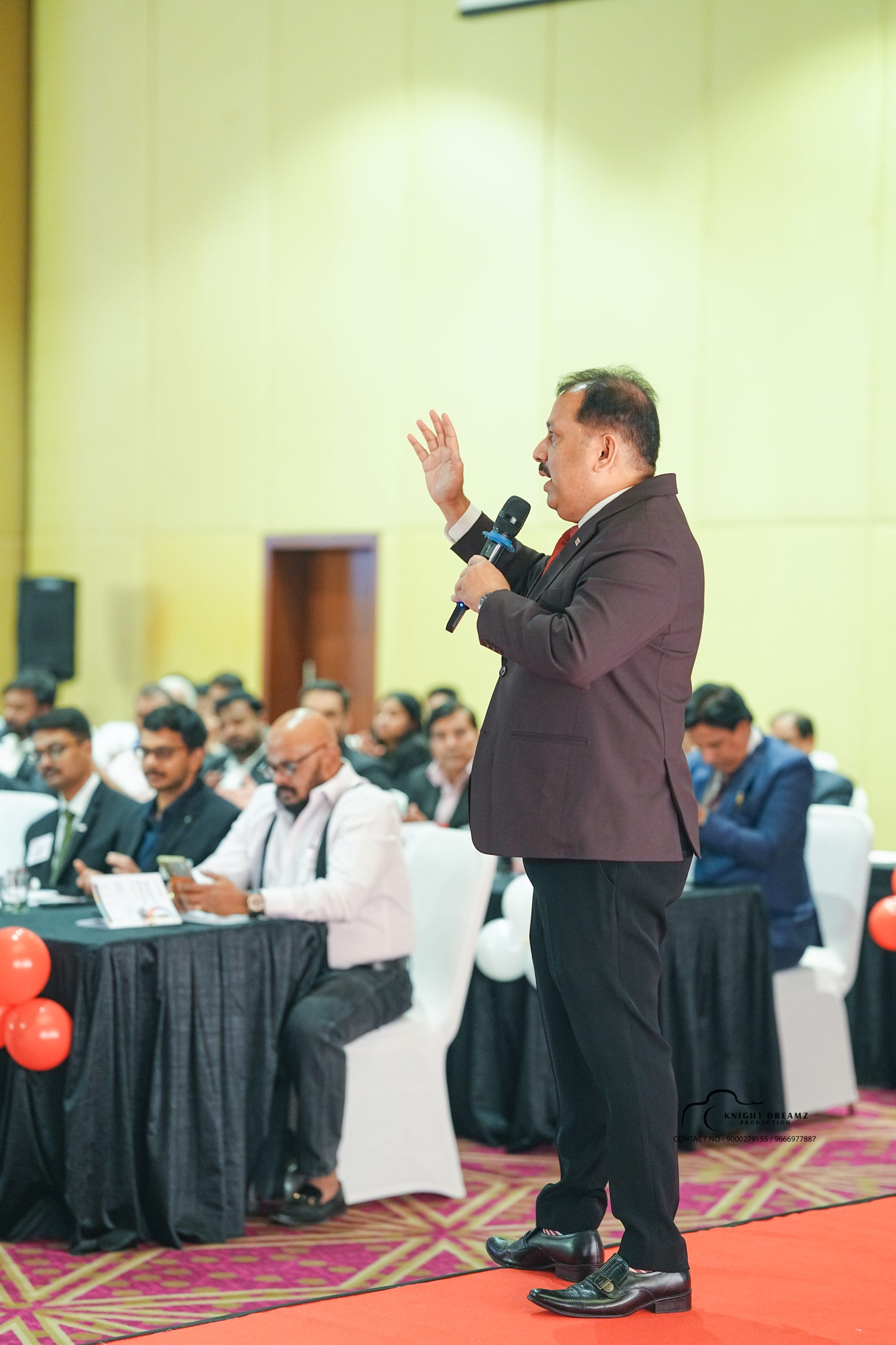 Uday Shetty full-length on stage speaking with audience behind